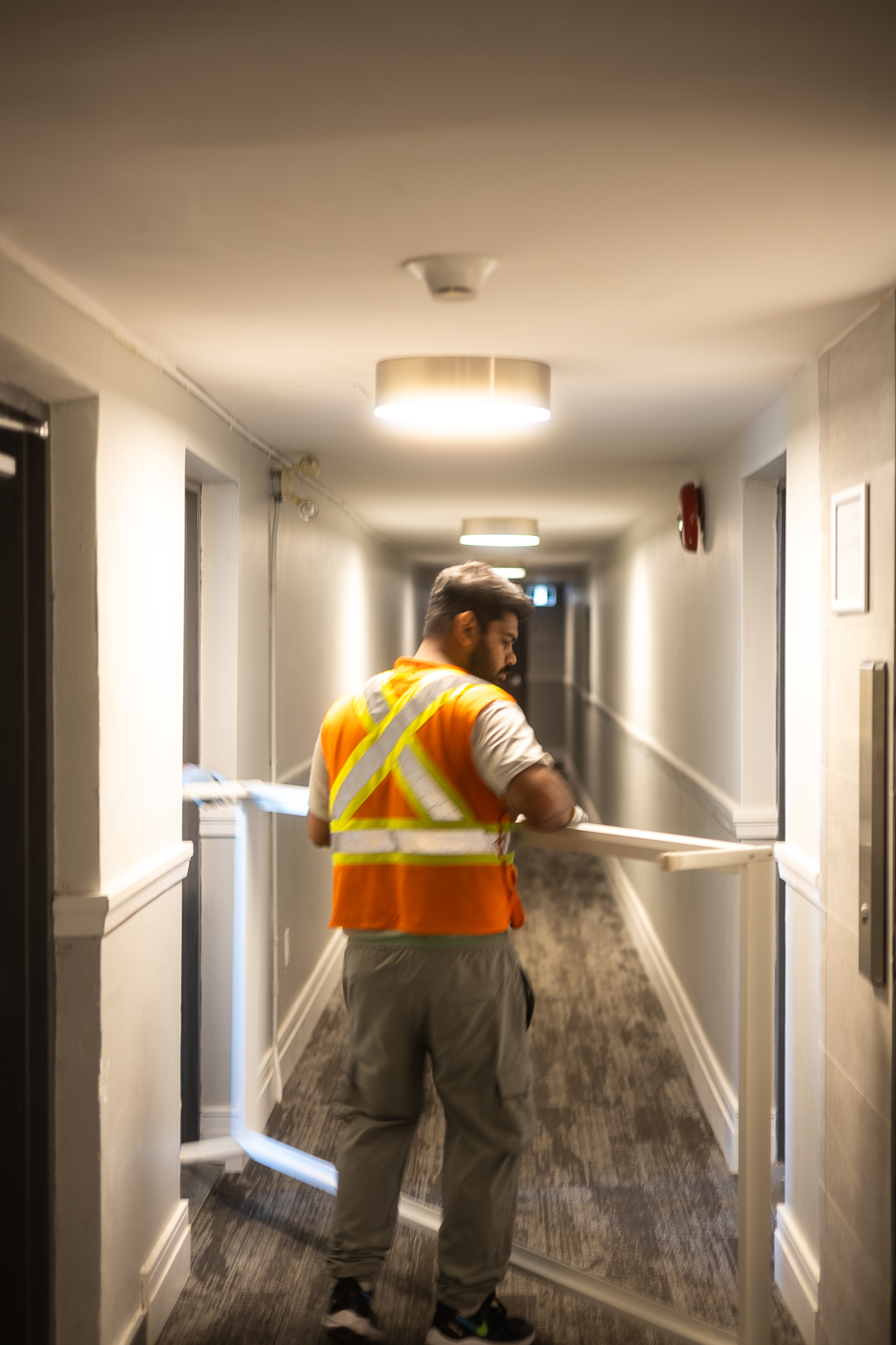 Rooster Movingz mover in a hi-vis vest carrying furniture through an apartment hallway